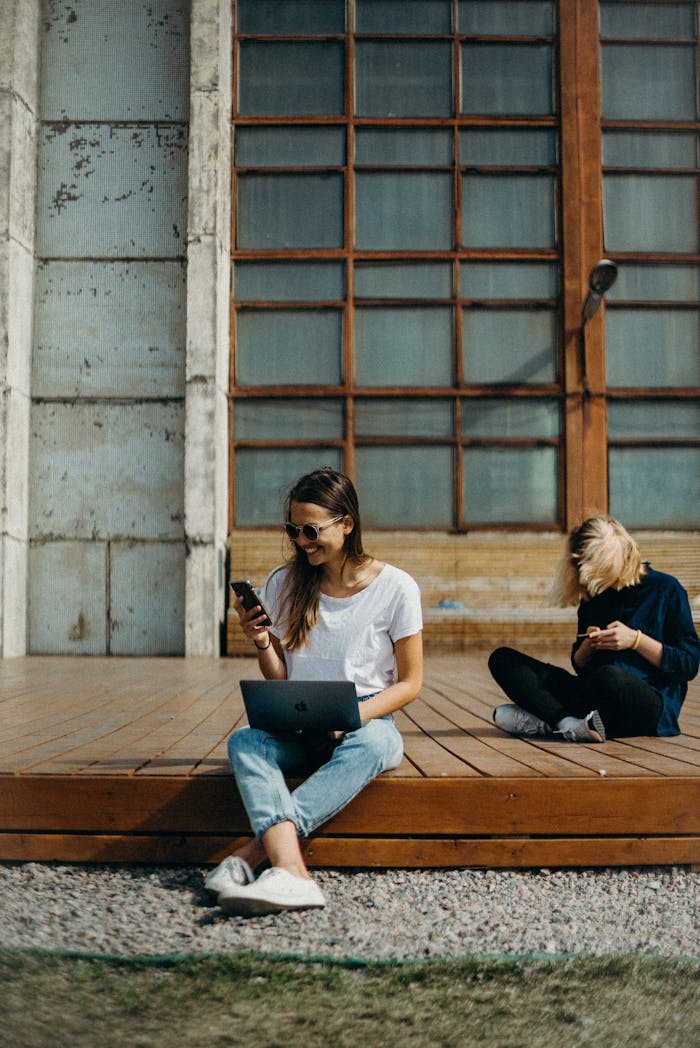 contact-img Two women working remotely on laptops outdoors, enjoying the sun. Perfect for freelance lifestyle themes.